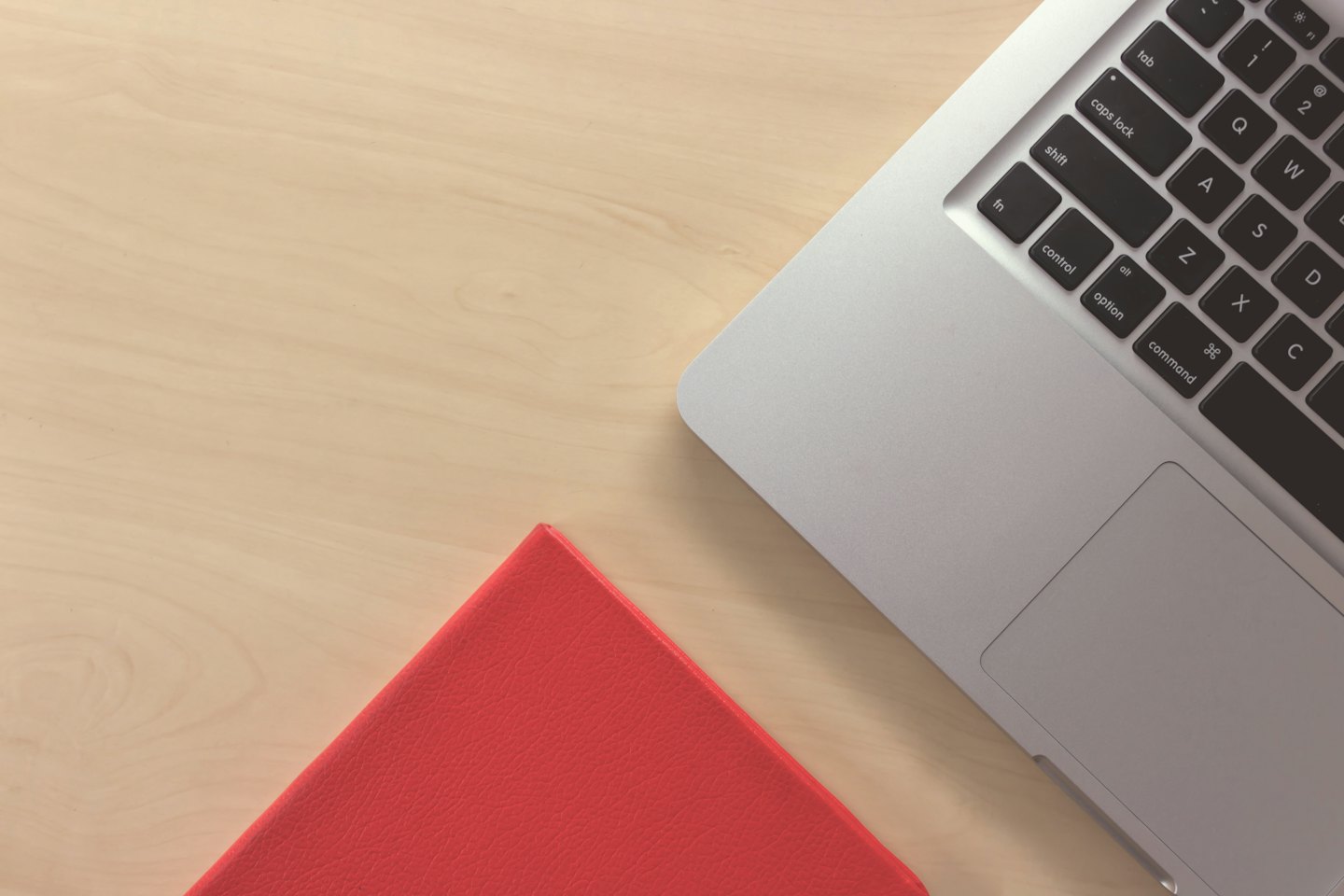 Laptop and red notebook on a wooden desk.